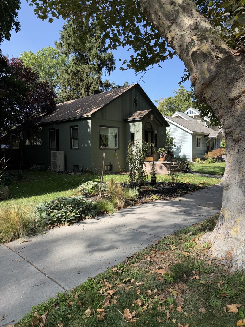 East side, viewed from the west. Opposite oblique showing the long stucco wall, asphalt-shingle roof, brick chimney, and entrance bay.