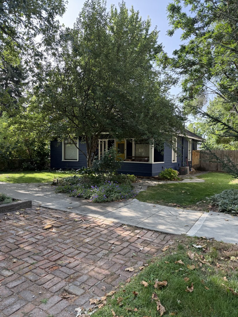 North side, viewed from the south. Oblique front view of the clapboard cottage and recessed porch beneath tree cover.