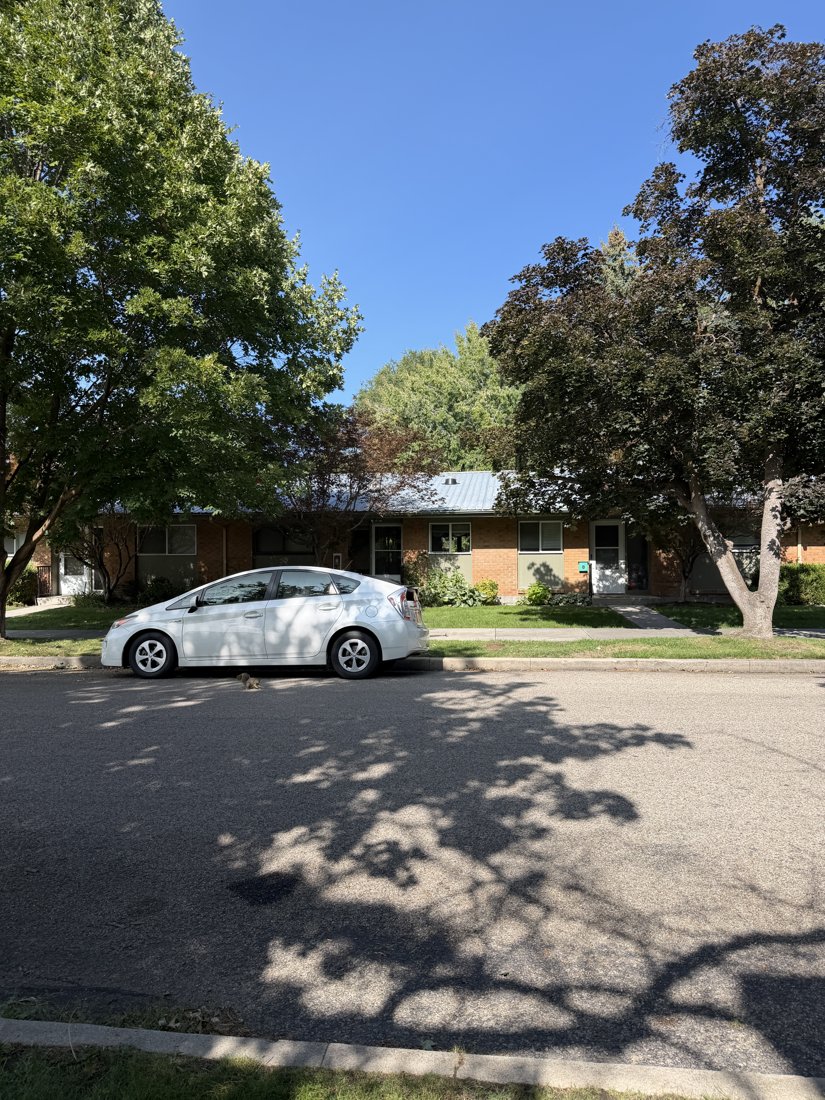 South and east sides, viewed from the northwest. Additional entrances and windows along the brick frontage, partly obscured by a parked car and trees.