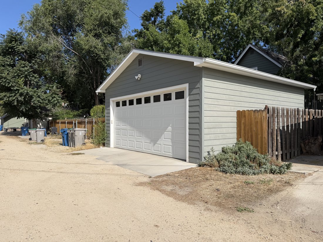 East side, viewed from the west. Alley elevation of a garage with a front gable, horizontal siding, and wide overhead door.