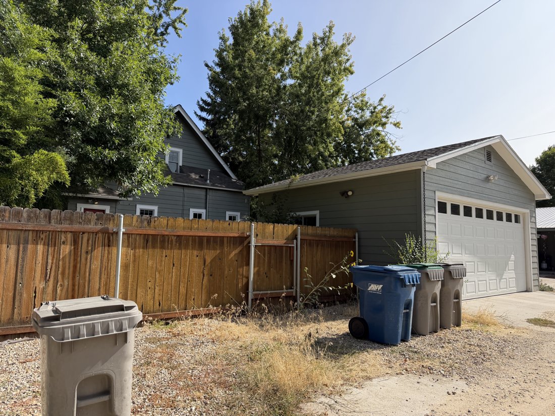 South and west sides, viewed from the northeast. Oblique garage view with the house visible behind the fence.