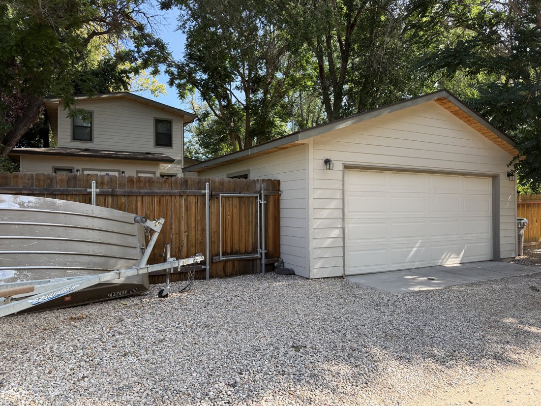 South and west sides, viewed from the northeast. Garage door elevation and rear of the house visible beyond the yard.