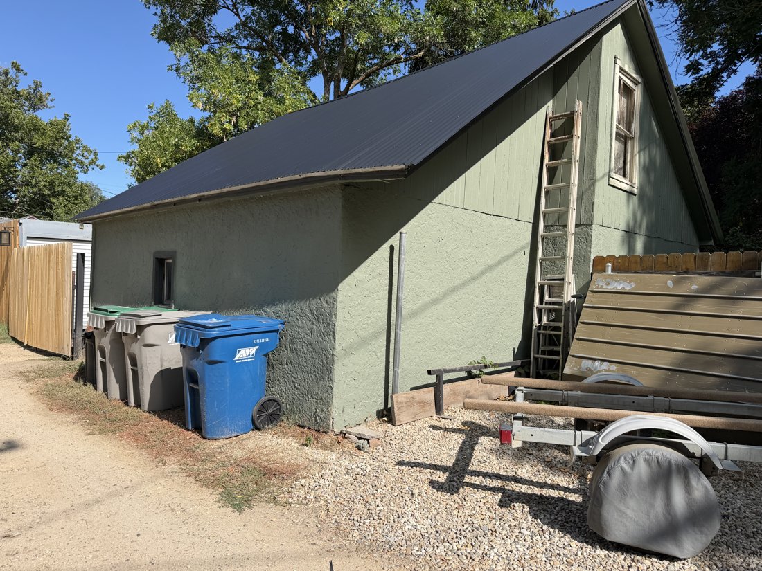 South side, viewed from the north. Gabled alley building with textured walls, vertical gable siding, narrow glazing, and metal roof.