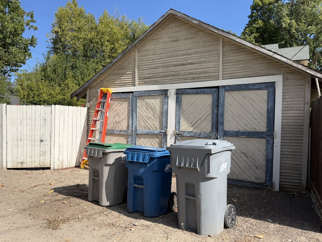 South and east sides, viewed from the northwest. Two-bay garage with two pairs of solid diagonal-board hinged doors and a clapboard gable.