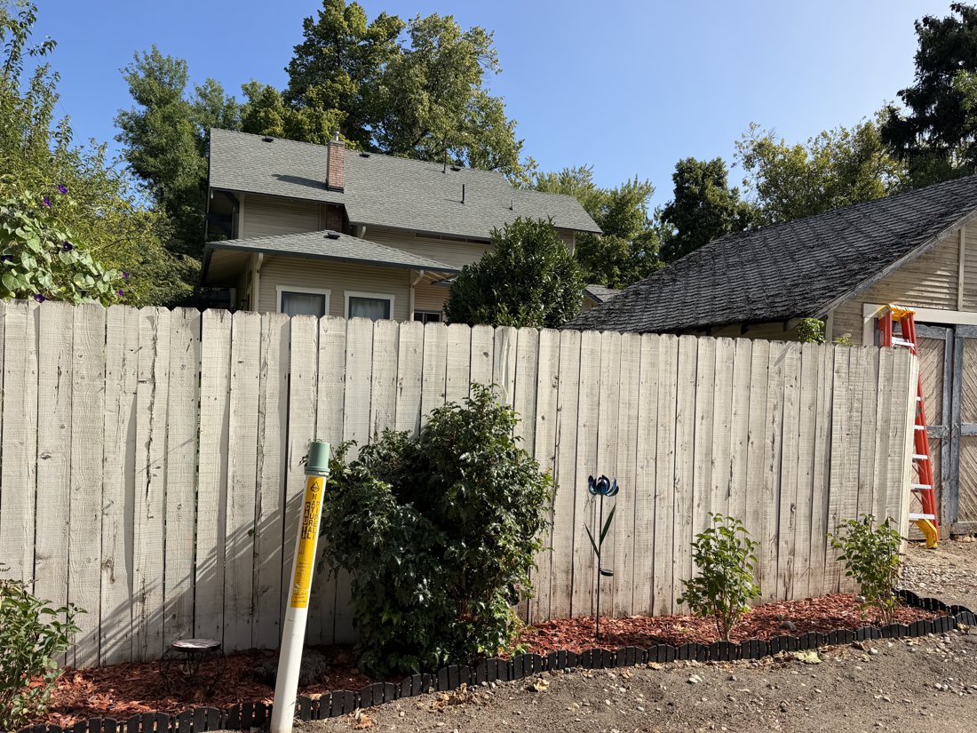 South and west sides, viewed from the northeast. Rear house with lower hipped-roof wing and brick chimney; probable garage wood-shingle roof visible above the fence.