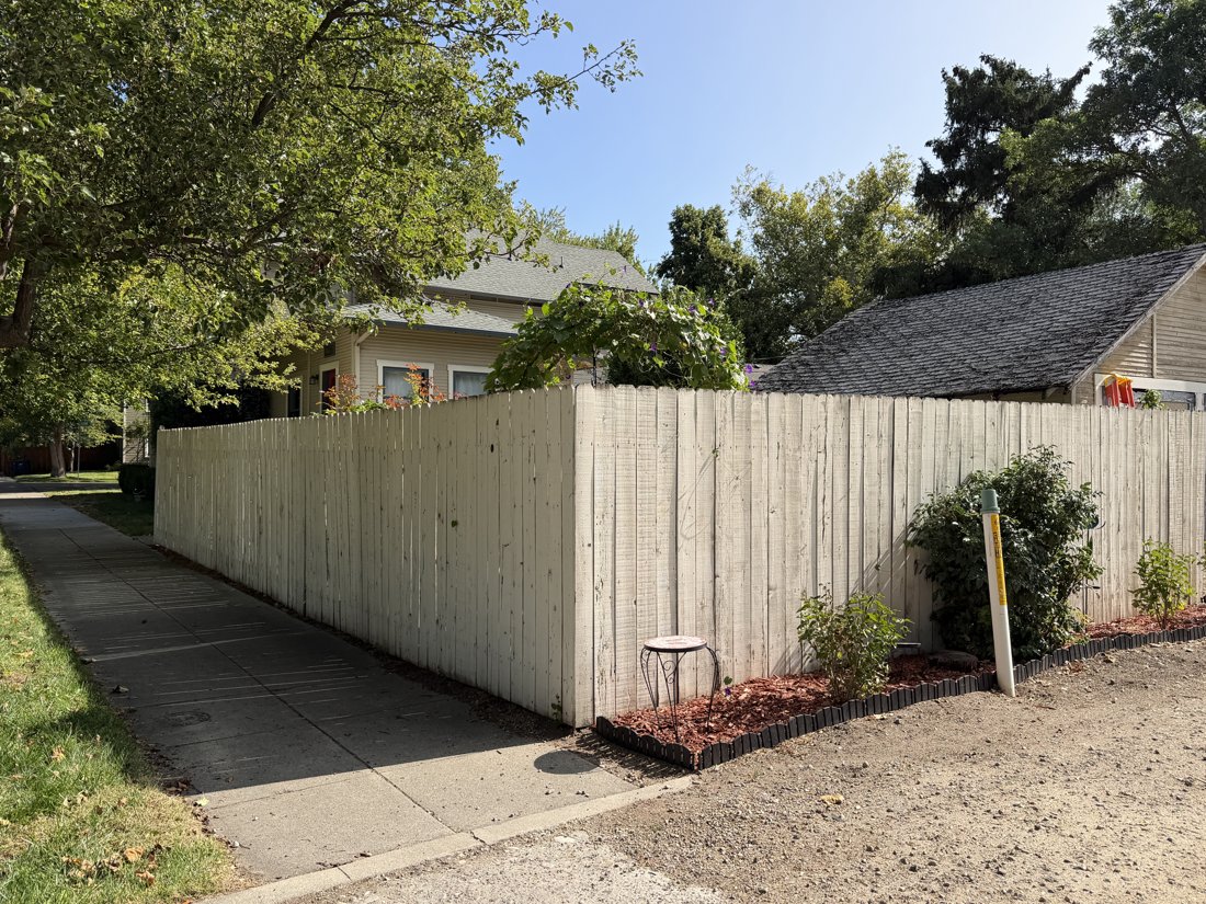 South and west sides, viewed from the northeast. Alley-to-side-yard view along the fence toward the house.