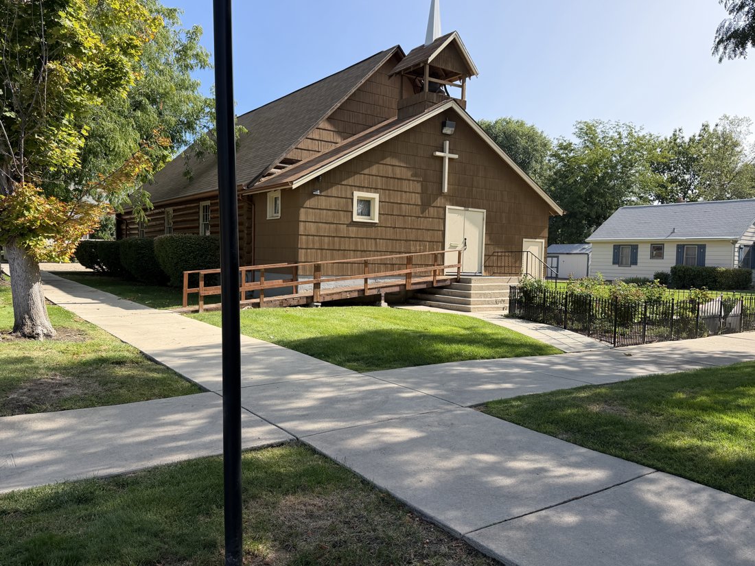 West side, viewed from the east. Church entrance oblique showing the wood access ramp, cross, shingled gable, and open belfry.