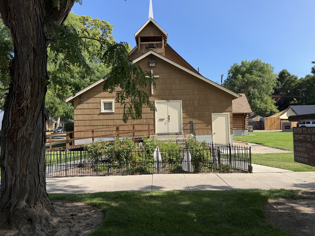 South and west sides, viewed from the northeast. Church entrance elevation with raised doorway, cross, front gable, and belfry.