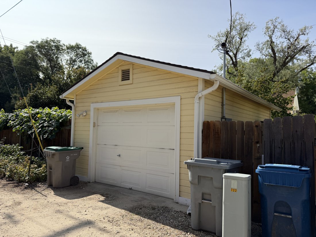 North side, viewed from the south. One-car garage with sectional door, horizontal lap siding, and rectangular gable vent.