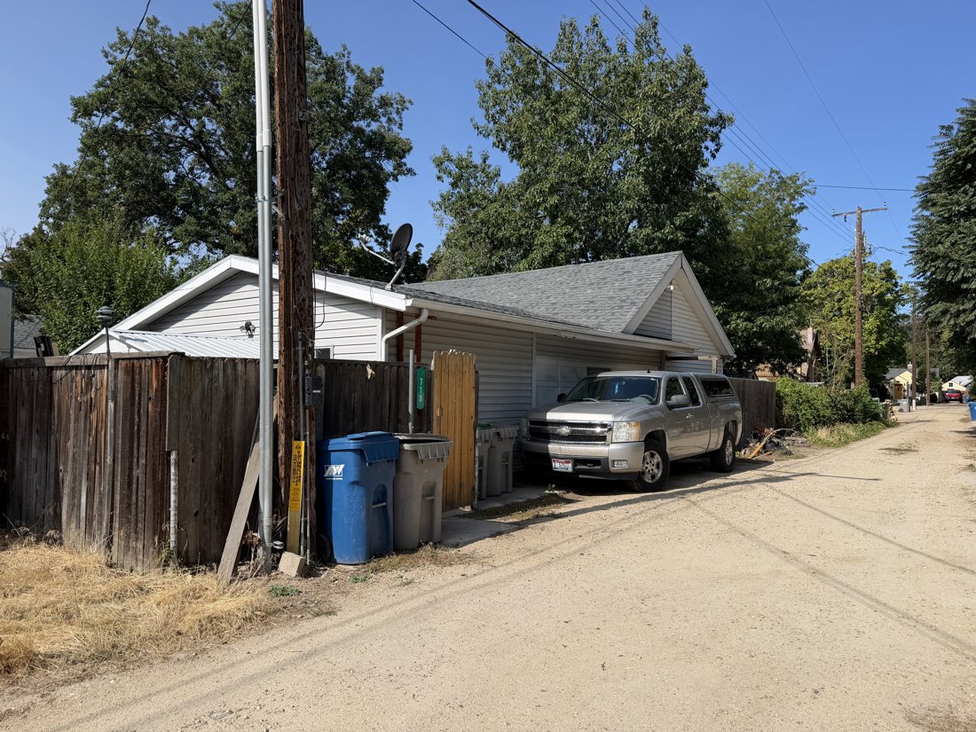 East side, viewed from the west. Oblique alley view of the rear garage or service building, gabled body, lower roof extension, and parked vehicle.