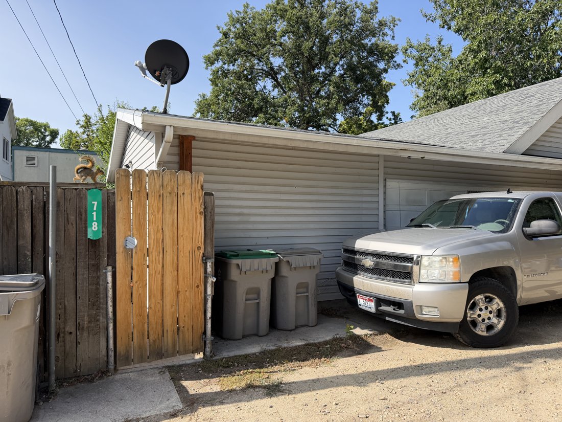 North and east sides, viewed from the southwest. Rear garage or service building with an address marker, apparent vinyl siding, and a partly screened sectional garage door.