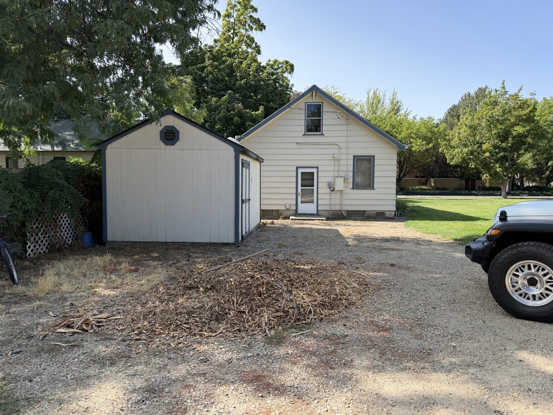 North and east sides, viewed from the southwest. Rear house and probable shed with vertically grooved panels and octagonal gable vent; concrete house base visible.